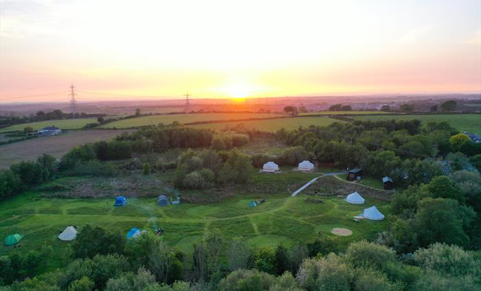 Birdseye view of the meadow camping area with tents and sunset in the distance over Anglesey